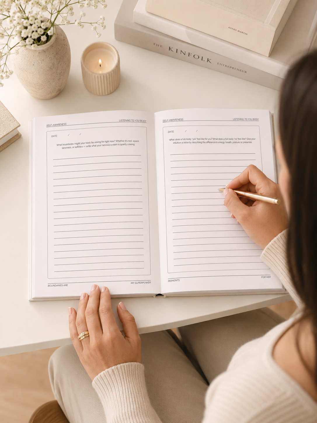 woman writing in a prompted self-love journal with a candle , flowers and books in the background
